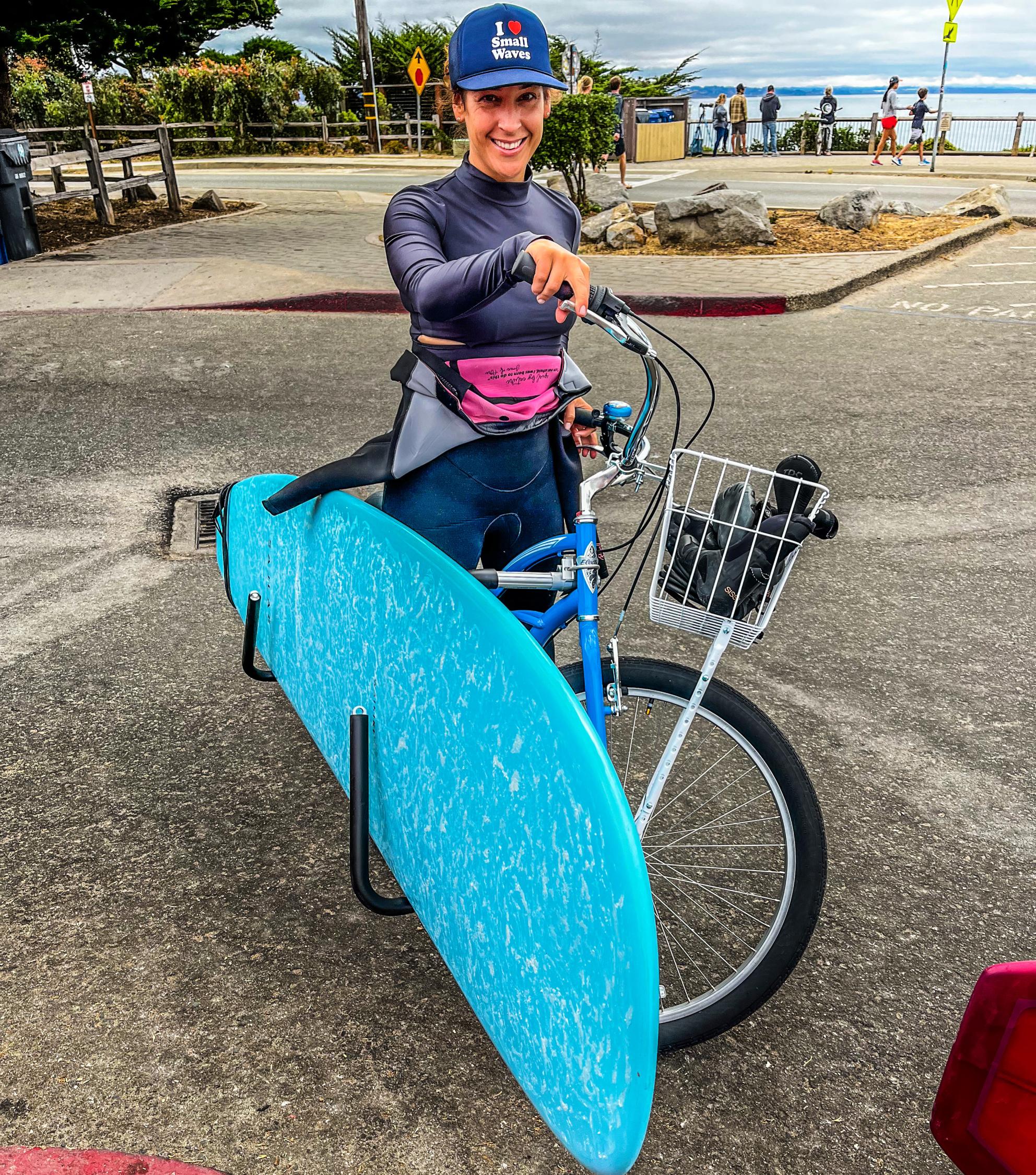 Suzanne DeLorenzo on her bike with a surf board 