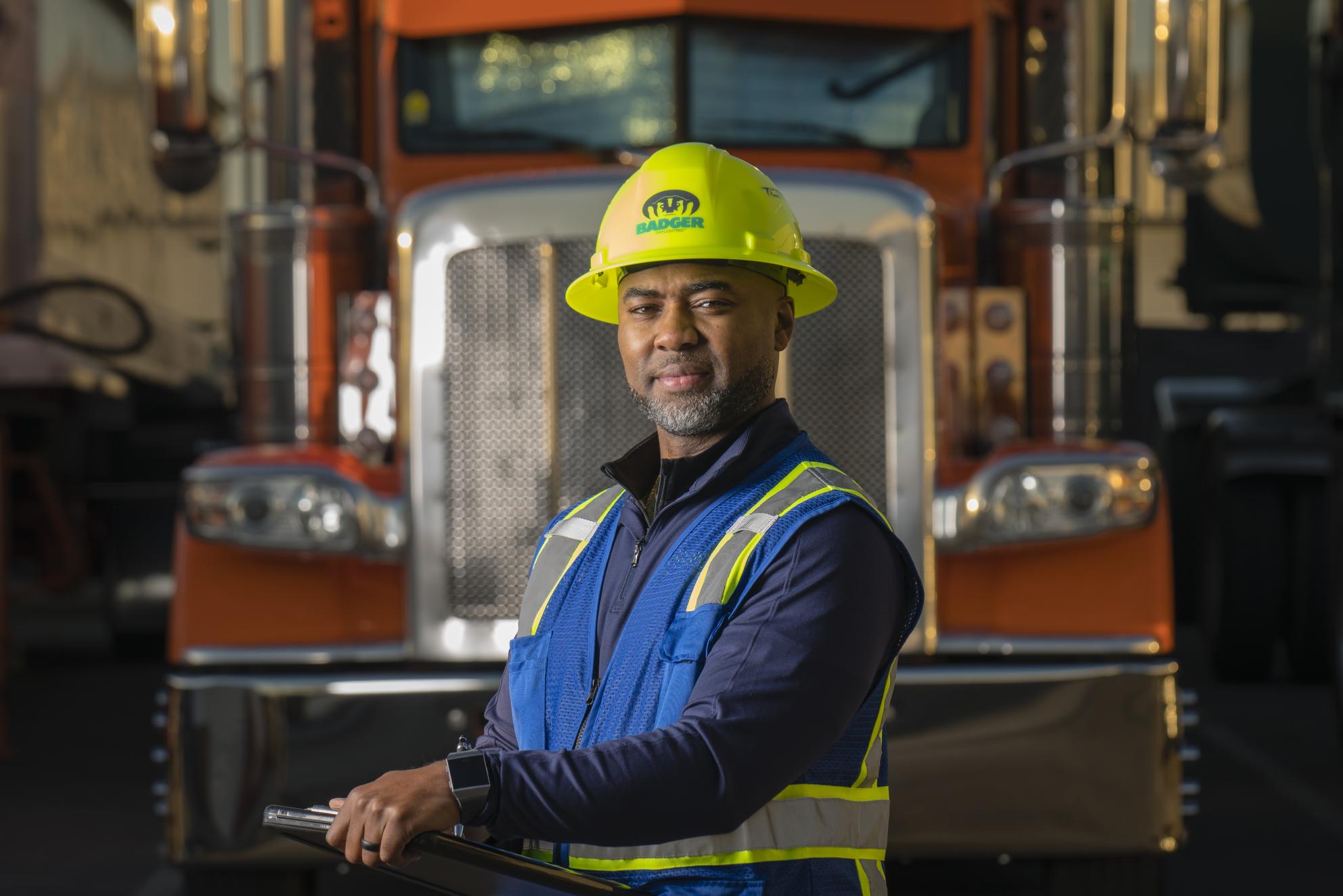 an employee looking at the camera holding a clip board in front of a truck