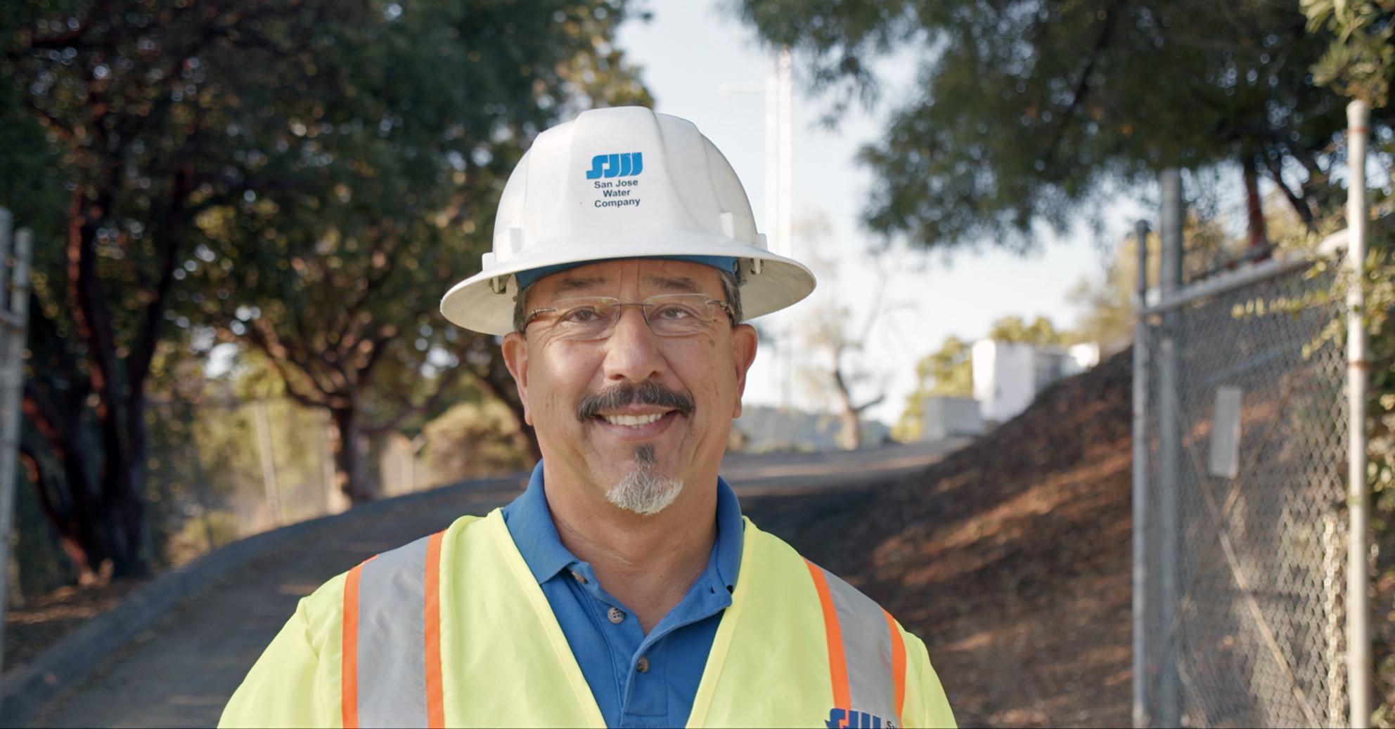 SJW employee with a hard hat and vest on looking at the camera