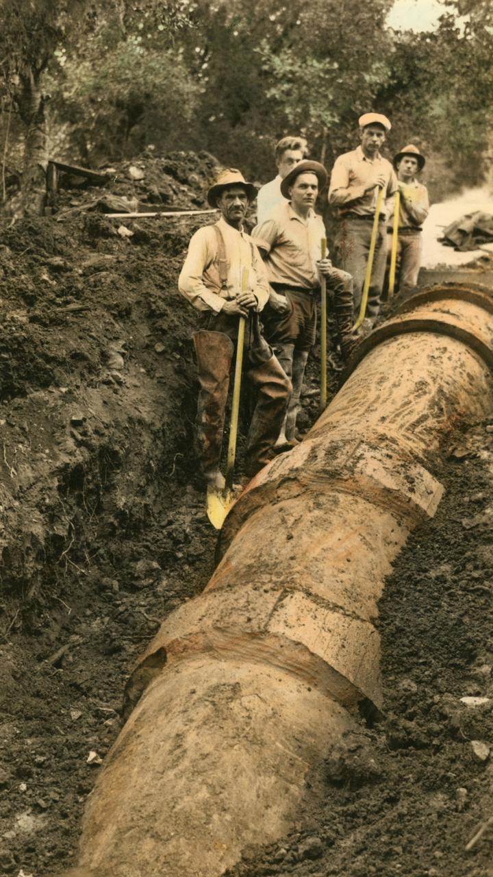 old photo of 5 people digging around a pipe