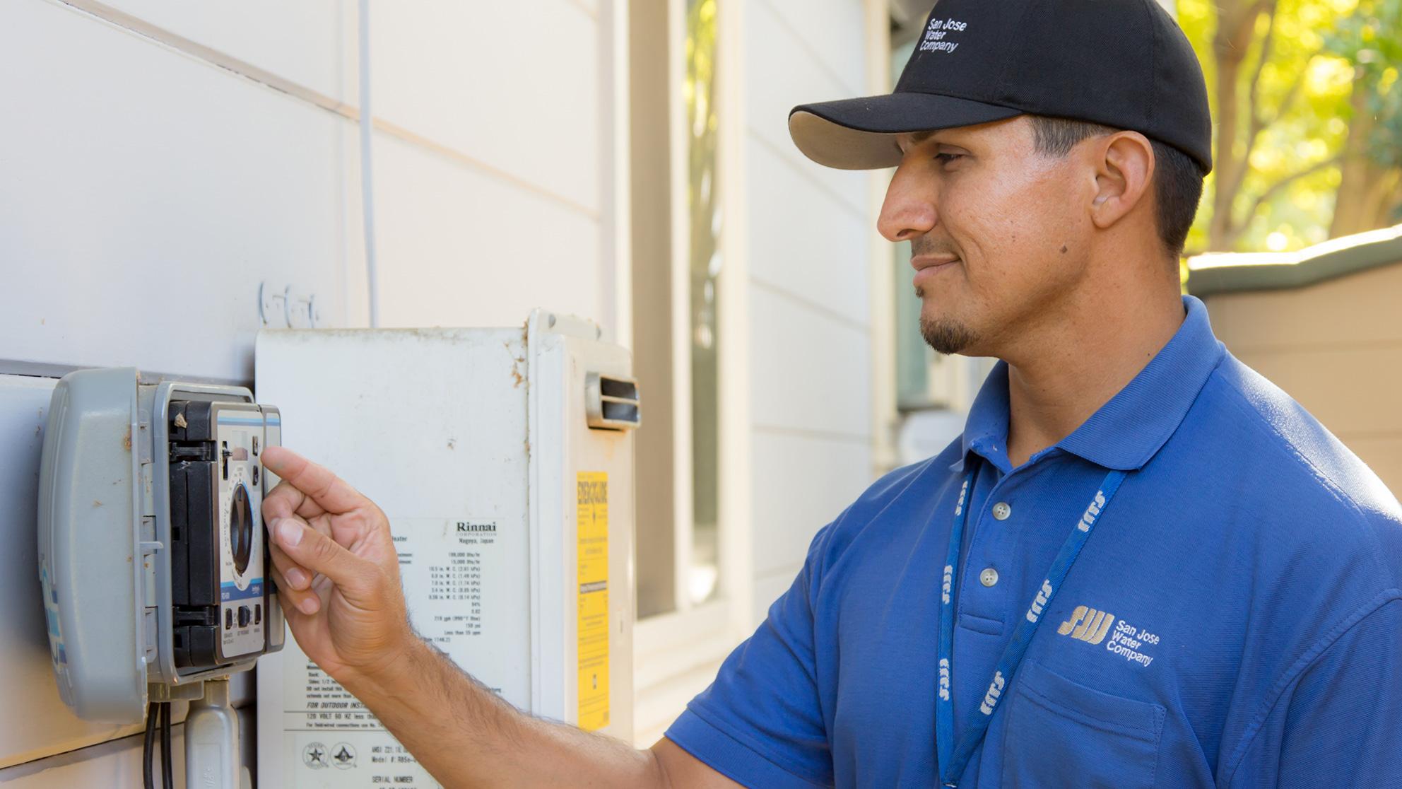 SJW service worker in blue shirt reading a water meter on the side of a house