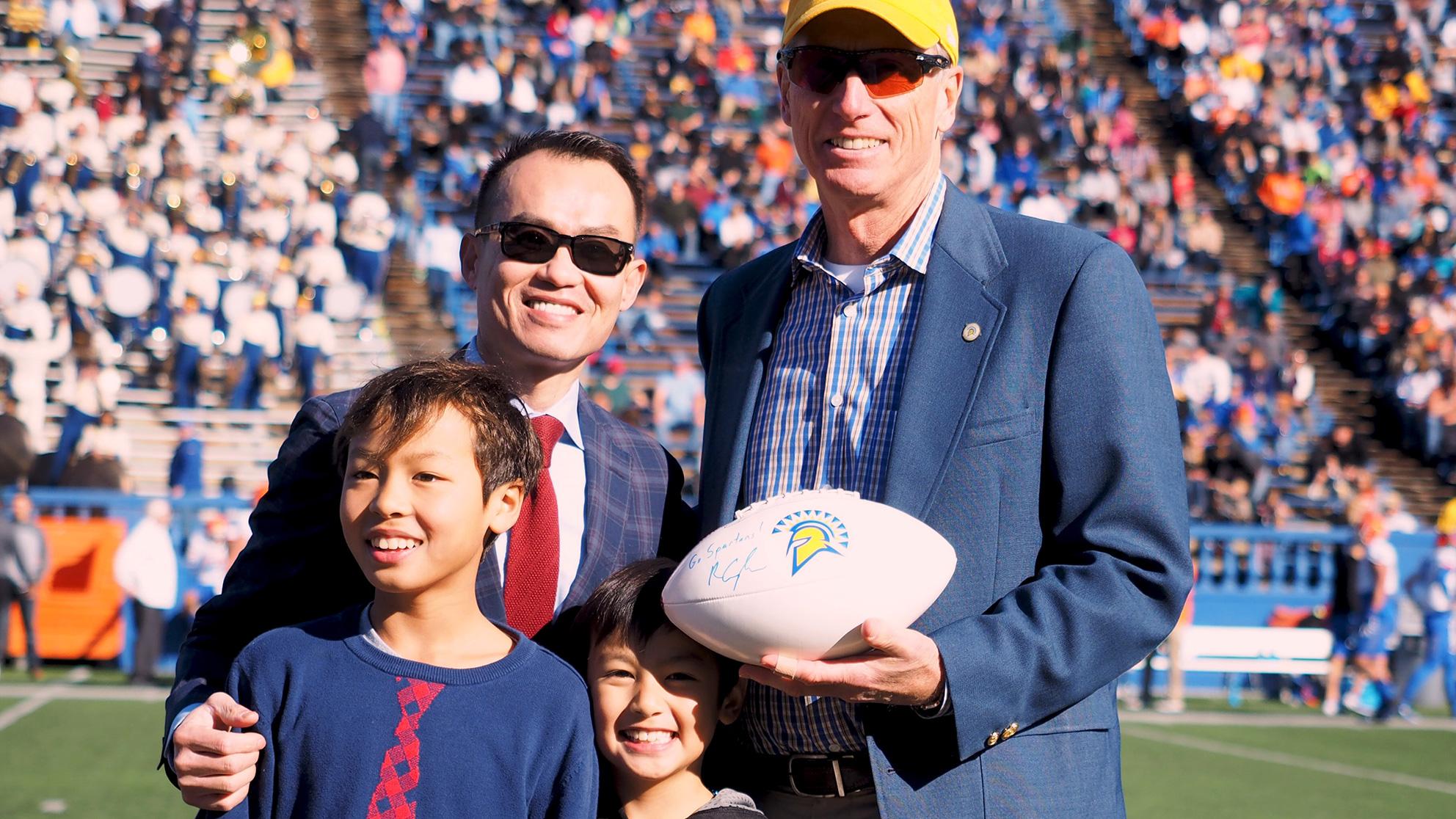 A father with his two young boys next to a tall man holding a football