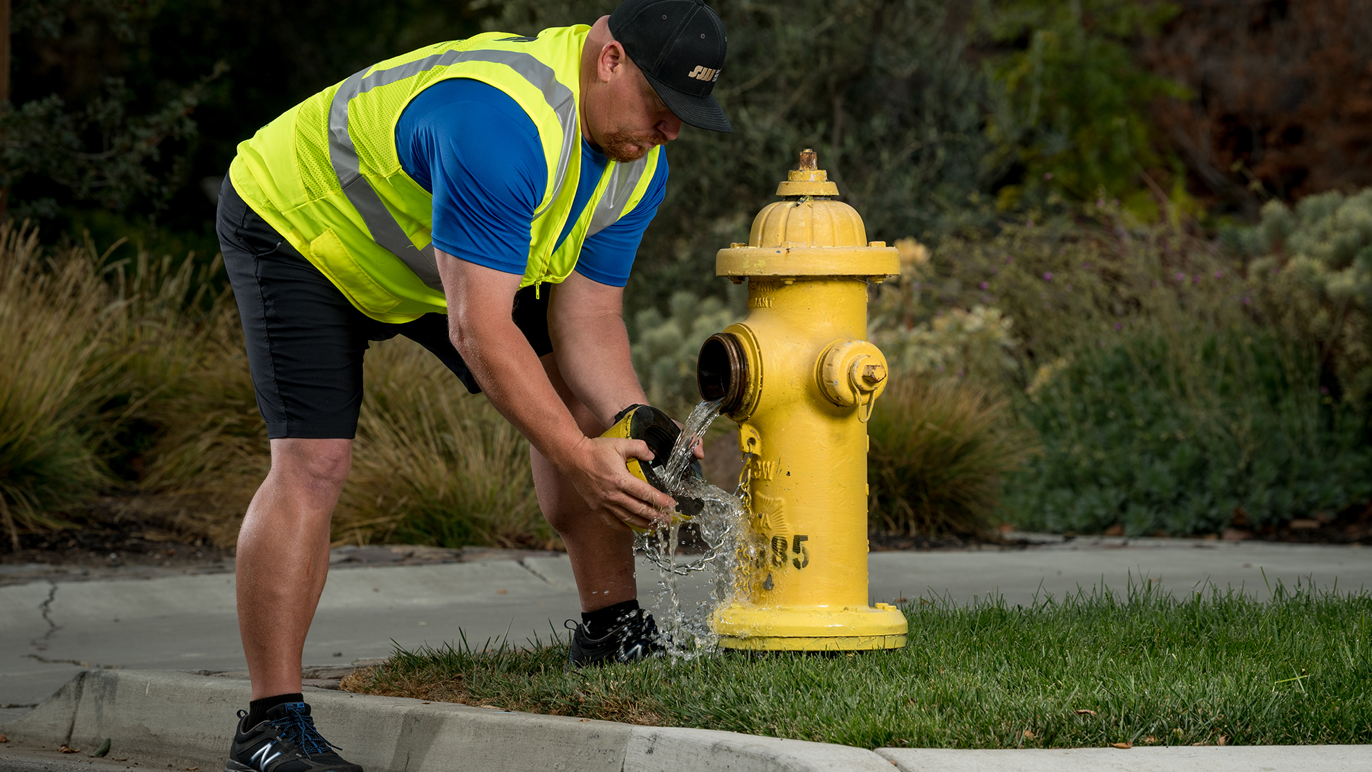 A San Jose Water employee removing the cap of a fire hydrant as some water leaks out.