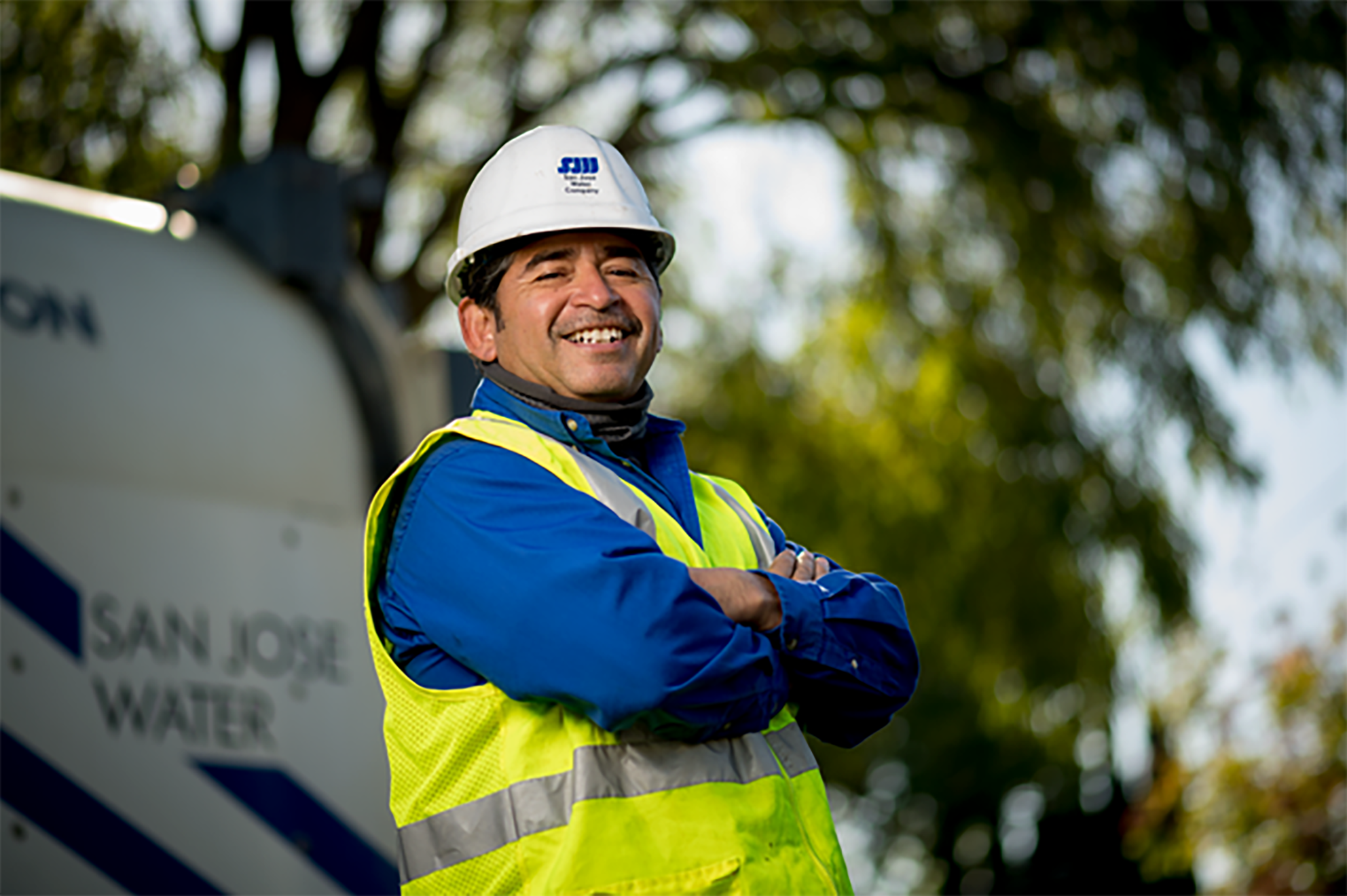 A male San Jose Water employee smiling with his arms cross in front of work truck.