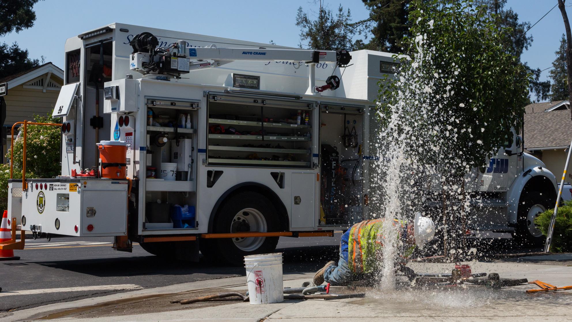 Worker kneeling down to fix a leak spraying water out of the ground