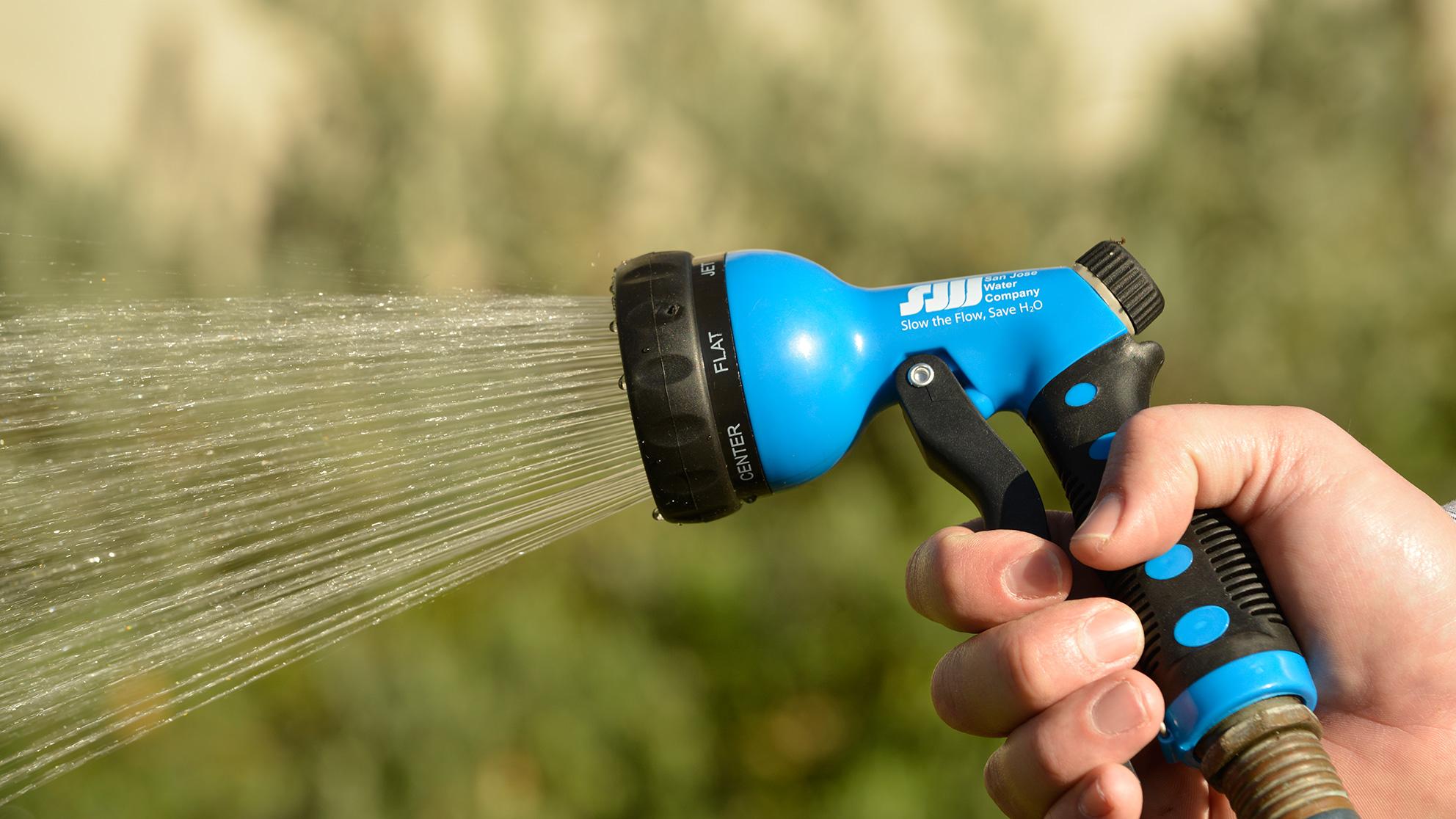 Hand holding a garden hose with blue nozzle spraying water