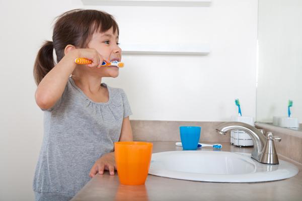 Little girl brushing her teeth with orange toothbrush and cup