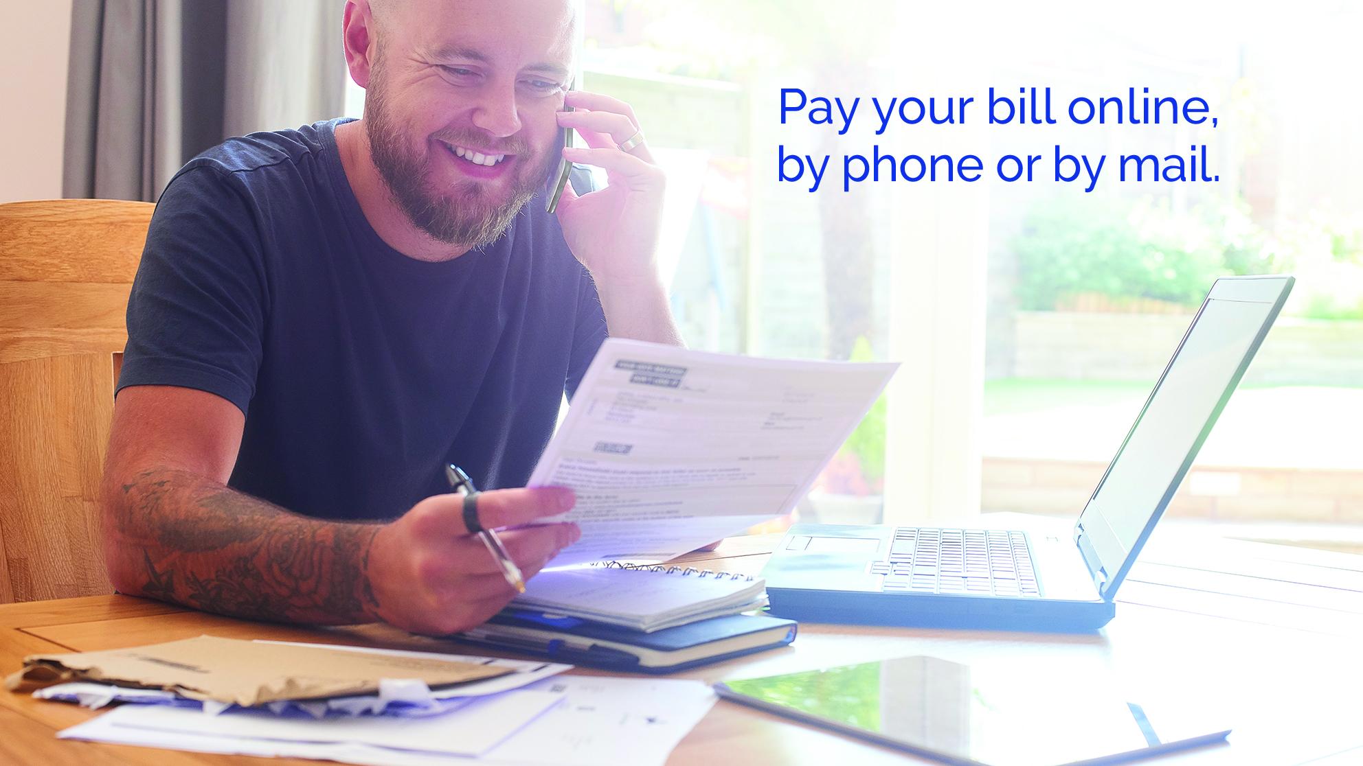 Man looking at his bill on the phone by the computer - Pay your bill online, by phone or by mail. 