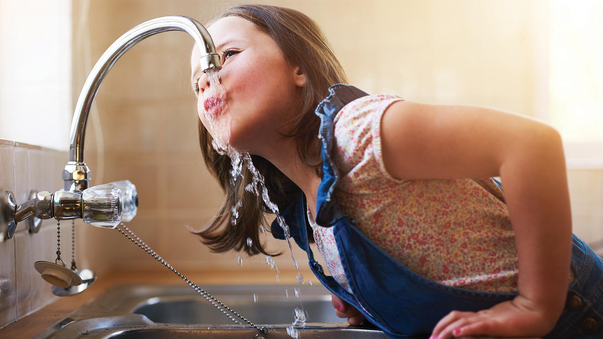 Child drinking water from kitchen sink faucet 