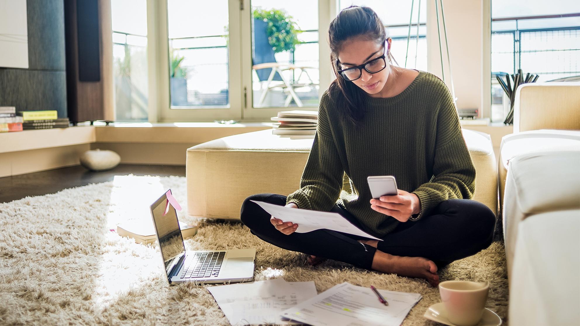 woman sitting on the floor with a laptop, paper and phone