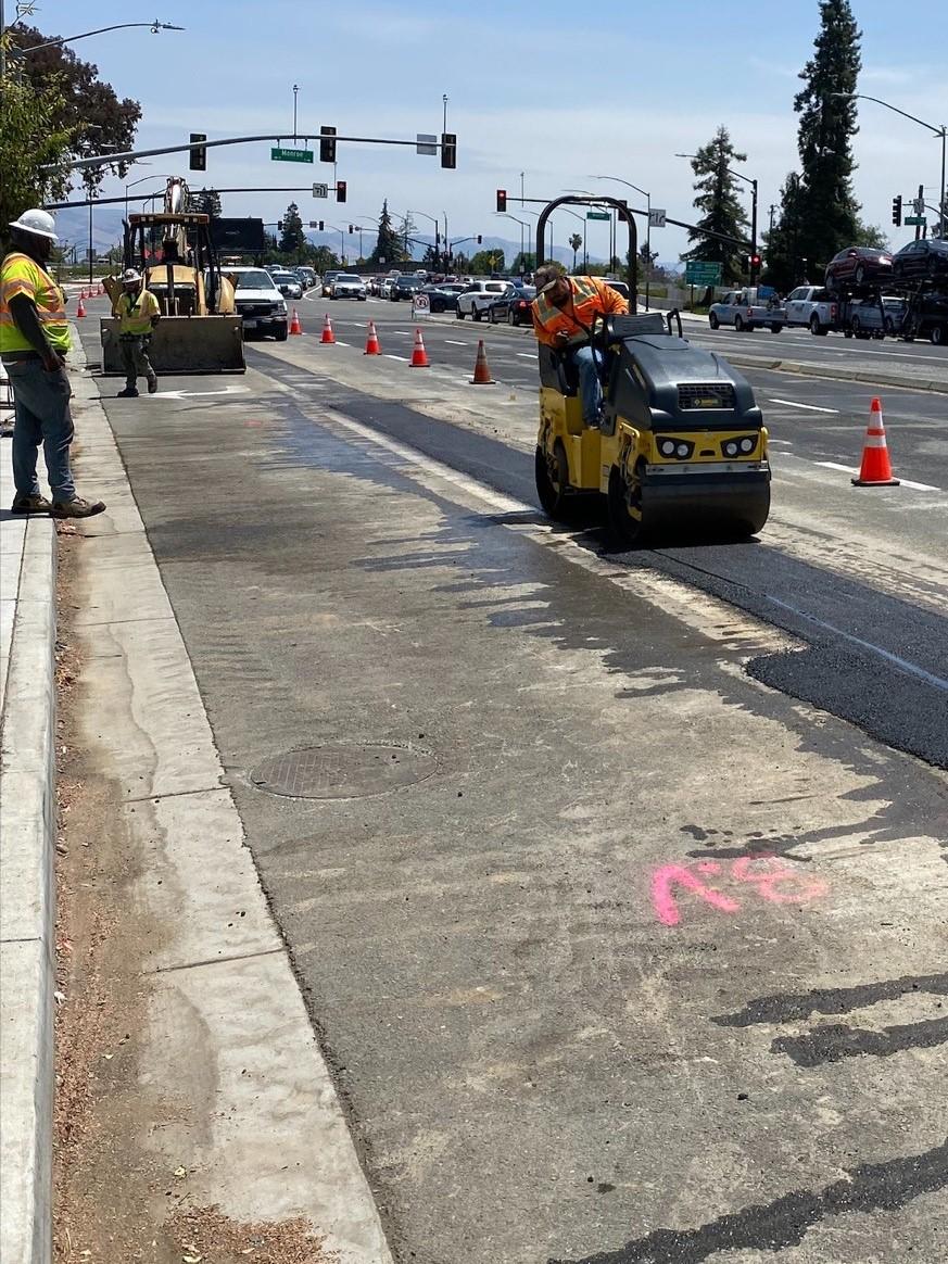 Worker on steam roller paving trench after water mains installed