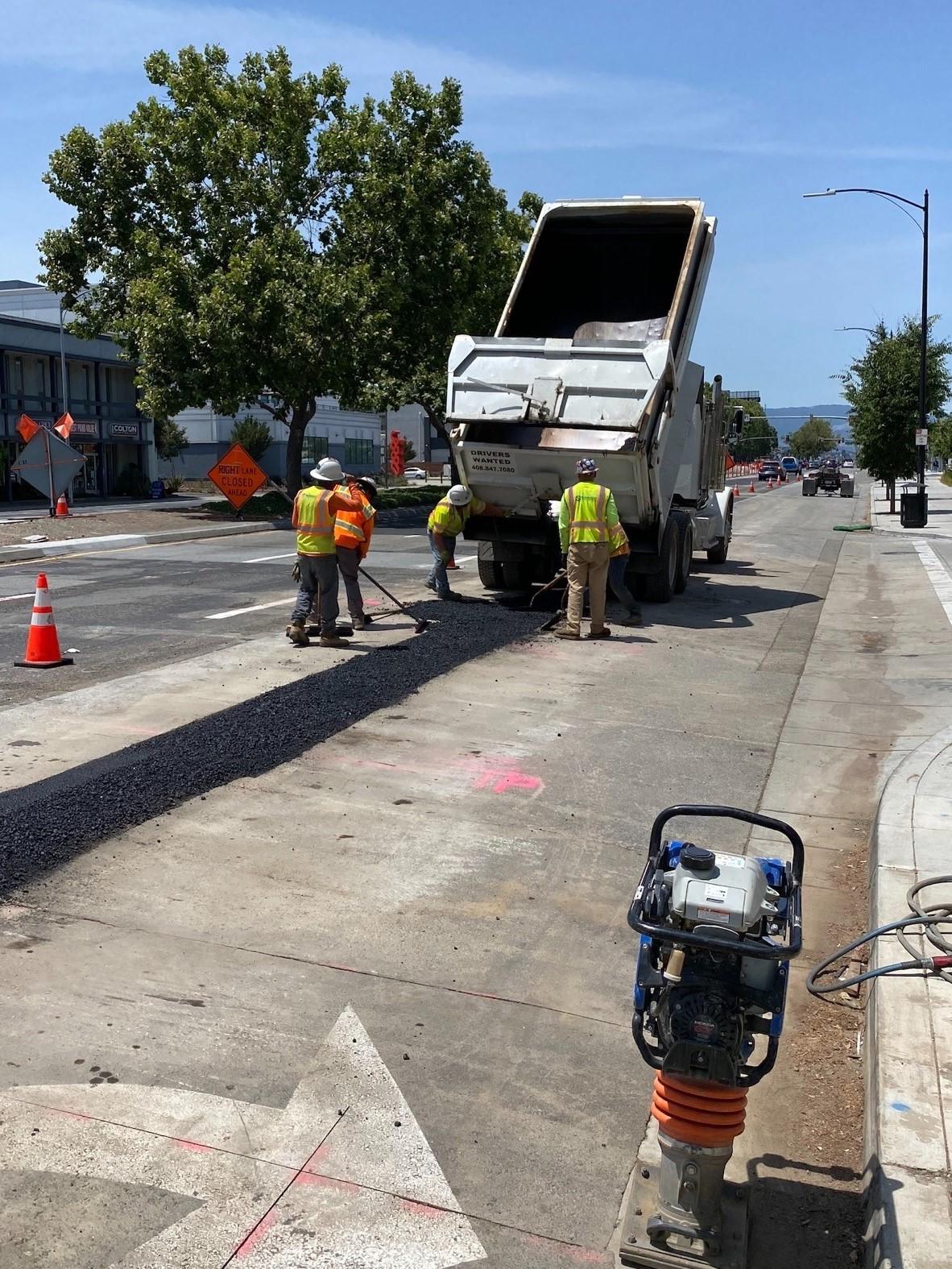 Dump truck emptying black top to trench in street