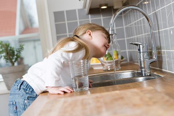 Little girl drinking water out of a kitchen faucet